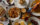 An overhead view shows an spread of a restaurant dishes, including roasted chicken, sandwiches, saucy shrimp, French fries and more.