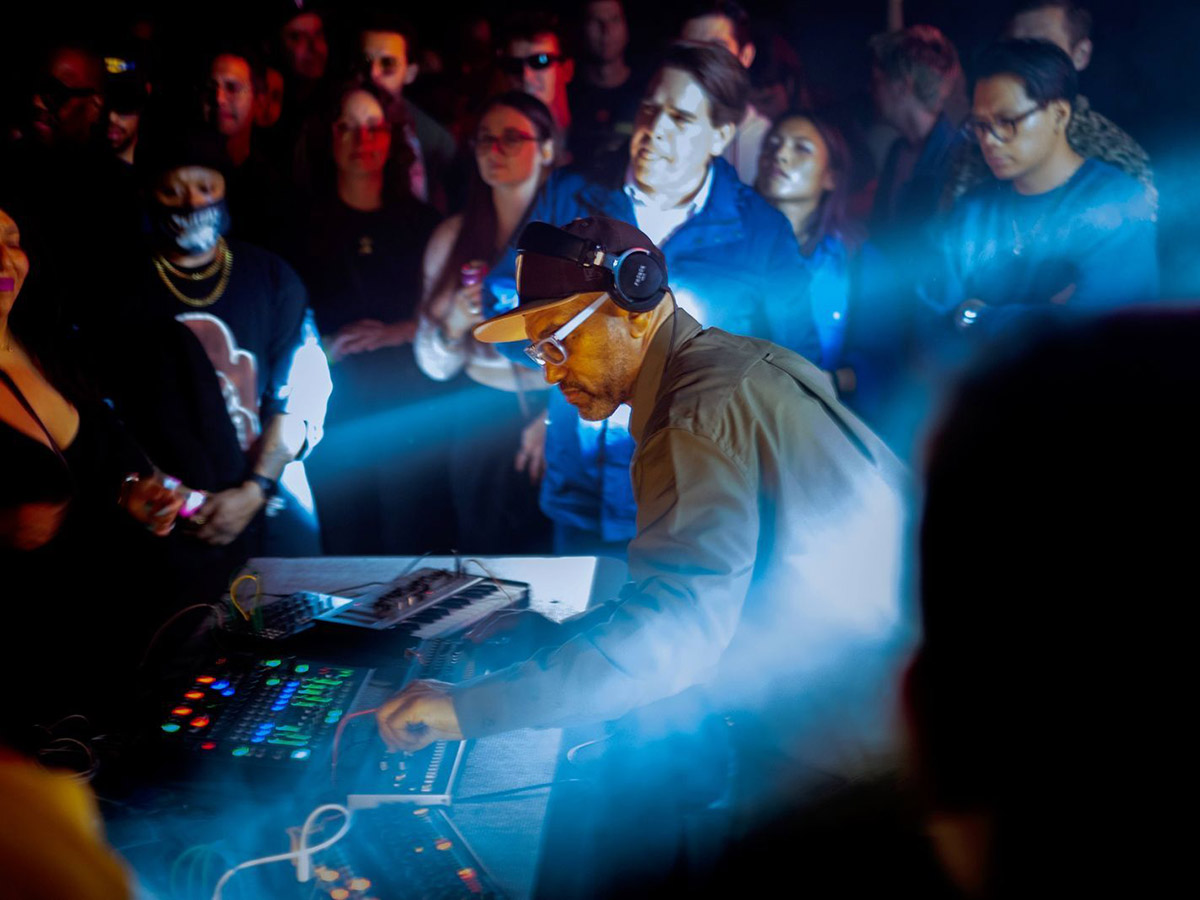 A headphones-wearing DJ performing in the middle of a small crowd, playing music and turning dials.