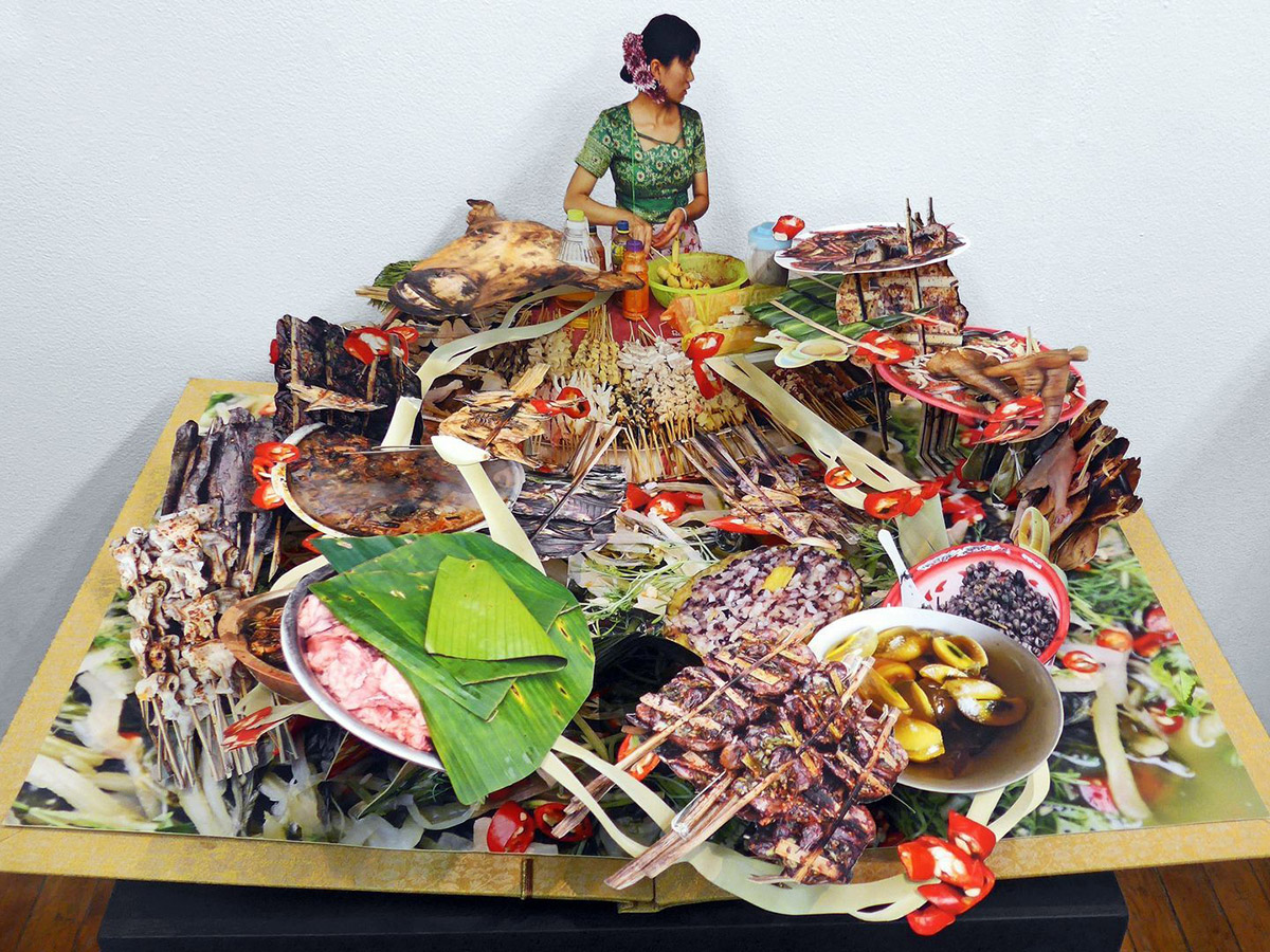 A large and vibrant pop-up book depicting Chinese cuisine, including soups, skewers and vegetables. The image of a woman in a green dress stands in the middle