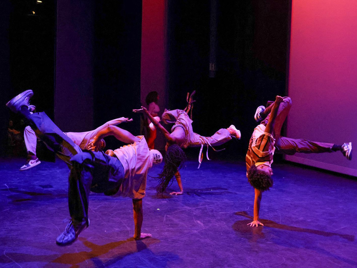A group of 4 performers breakdancing in unison, midair with hands on the floor