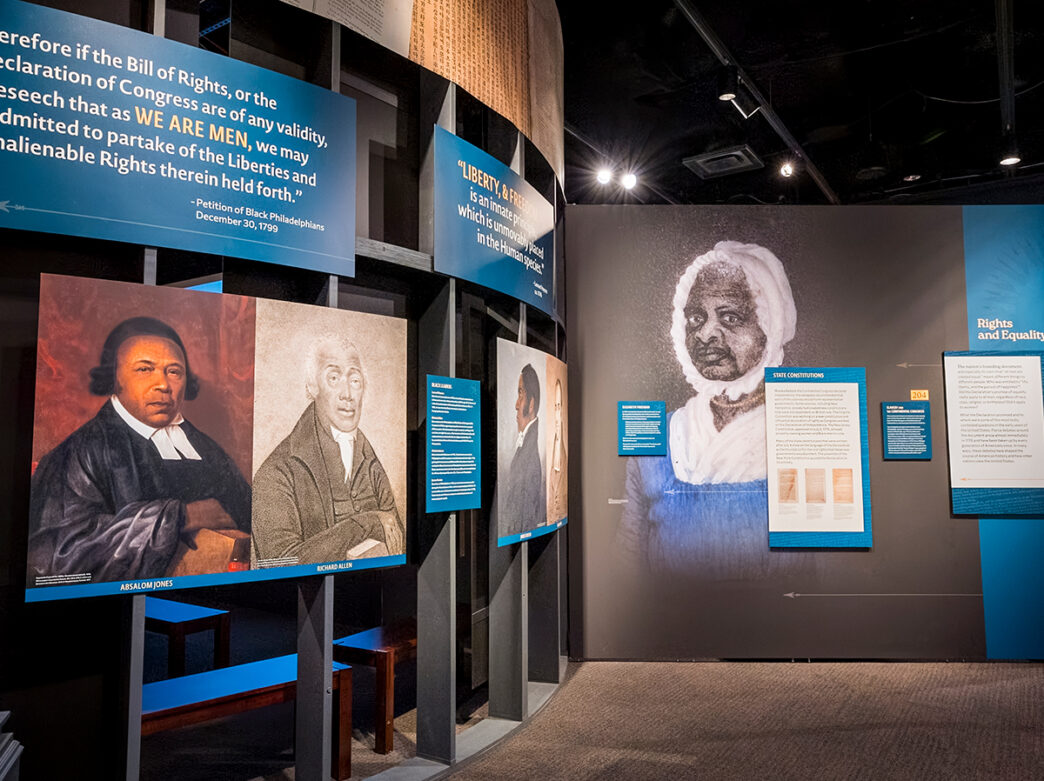 A gallery installation features portraits of Black historical figures alongside large blue text panels quoting 18th-century petitions for liberty and equality.