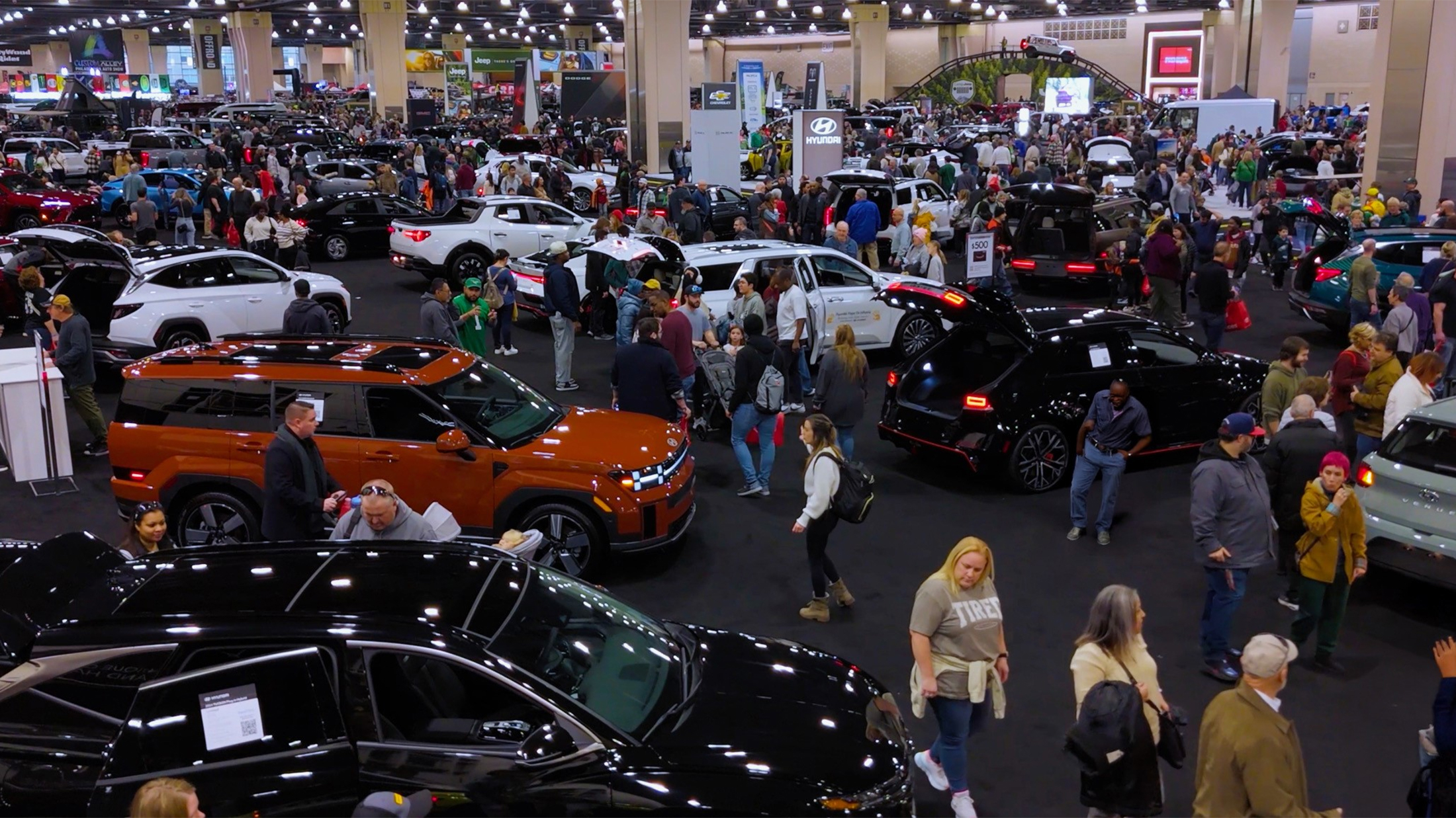 People walk through a busy convention center filled with new cars and SUVS at the Philadelphia Auto Show.