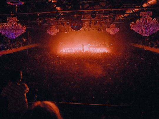 Las luces rojas y naranjas brillan desde el escenario del Fillmore Philadelphia, ante una gran multitud que observa.