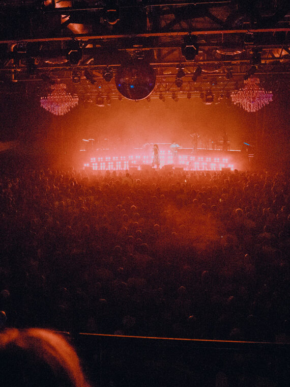 Red and orange lights glow from the stage at The Fillmore Philadelphia, with a large crowd watching