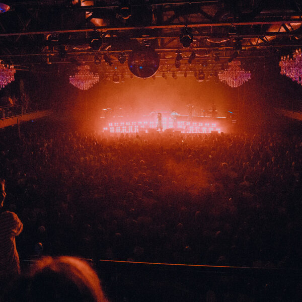 Red and orange lights glow from the stage at The Fillmore Philadelphia, with a large crowd watching