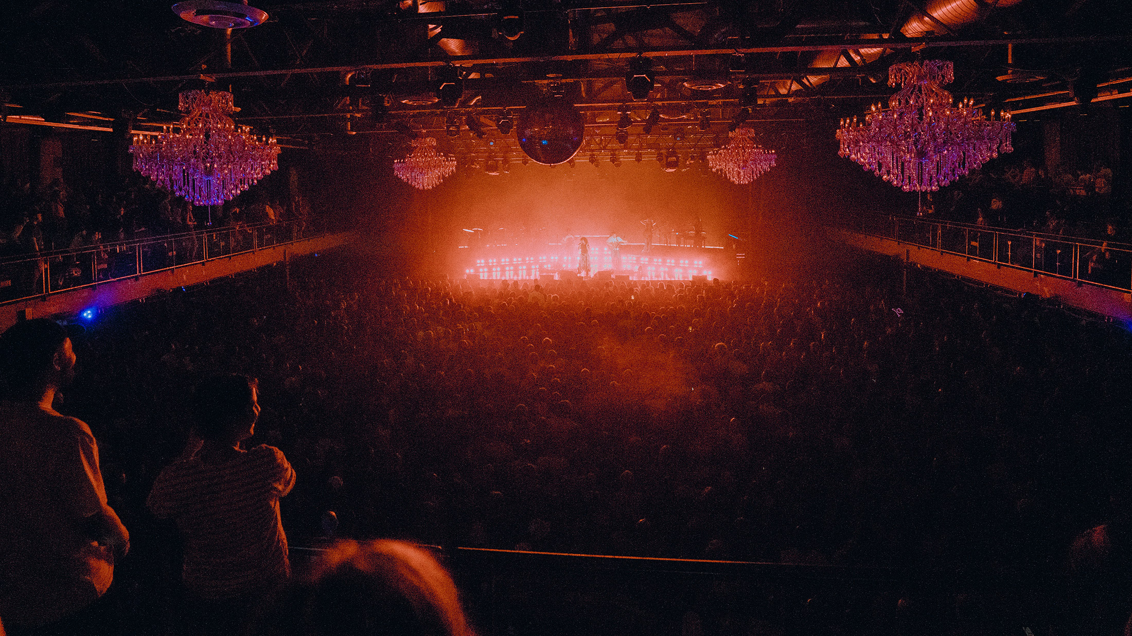 Las luces rojas y naranjas brillan desde el escenario del Fillmore Philadelphia, ante una gran multitud que observa.