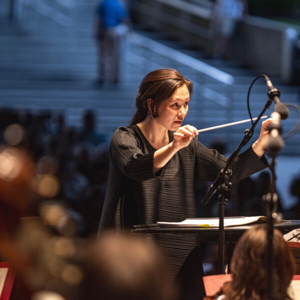 Philadelphia Orchestra conductor waving her baton at an open air concert at Highmark Mann. Players are in the foreground