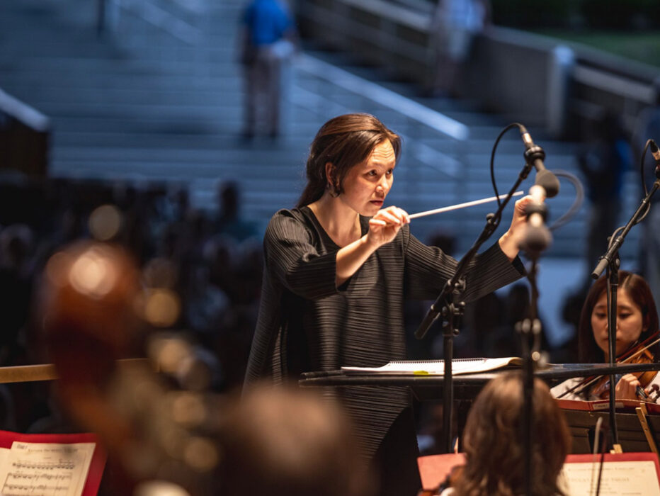 Philadelphia Orchestra conductor waving her baton at an open air concert at Highmark Mann. Players are in the foreground