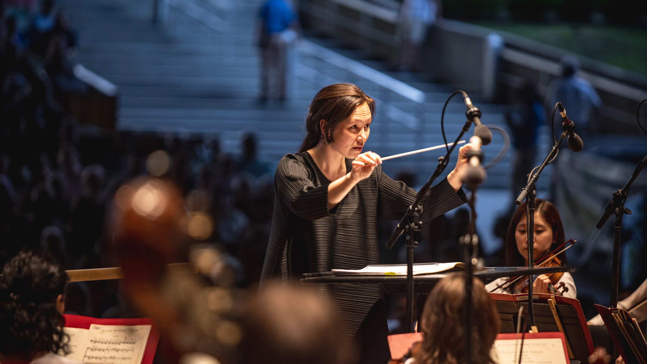 Philadelphia Orchestra conductor waving her baton at an open air concert at Highmark Mann. Players are in the foreground