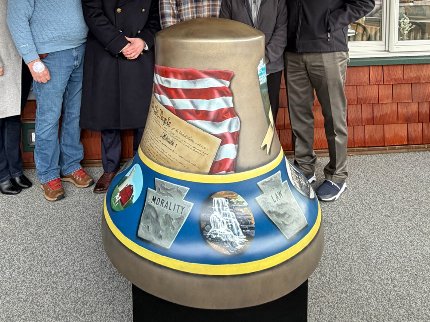 A painted fiberglass Liberty Bell sculpture features imagery of the American flag, the Constitution and stone tablets, with people standing behind it during a public display.