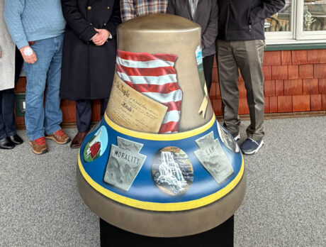 A painted fiberglass Liberty Bell sculpture features imagery of the American flag, the Constitution and stone tablets, with people standing behind it during a public display.