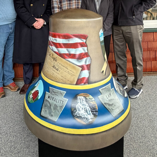A painted fiberglass Liberty Bell sculpture features imagery of the American flag, the Constitution and stone tablets, with people standing behind it during a public display.