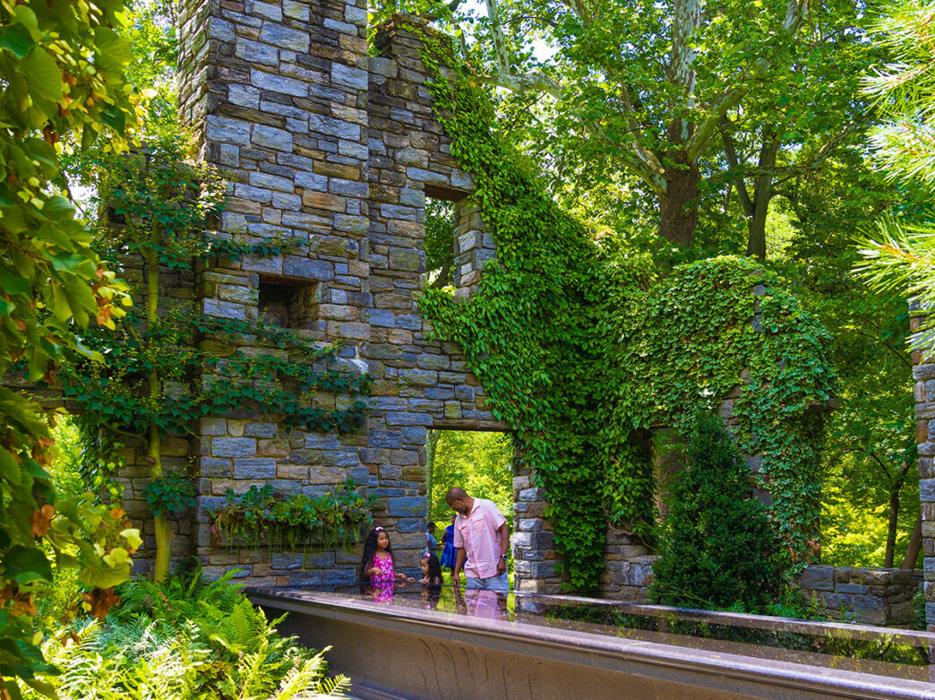 A family explores a vine-covered stone ruins and vibrant gardens.