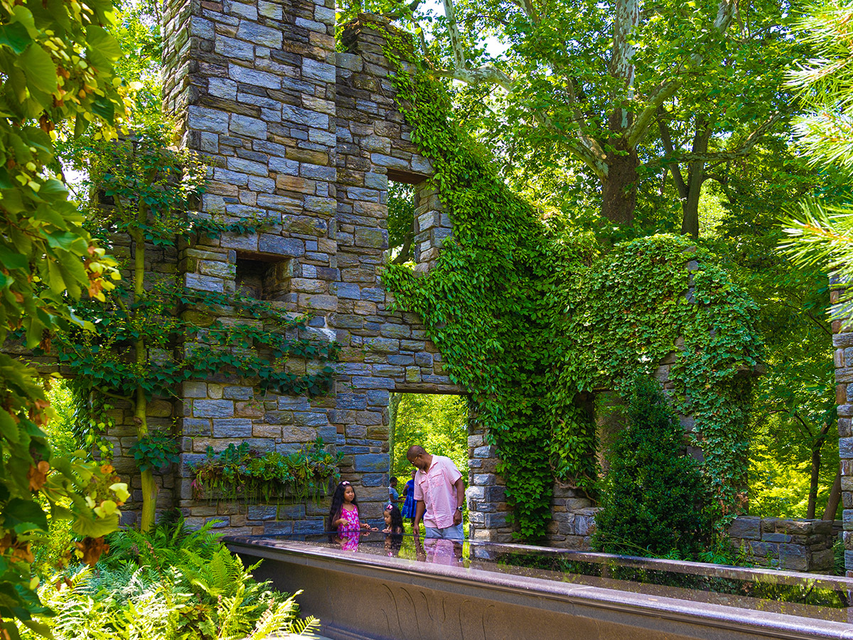 A family explores a vine-covered stone ruins and vibrant gardens.