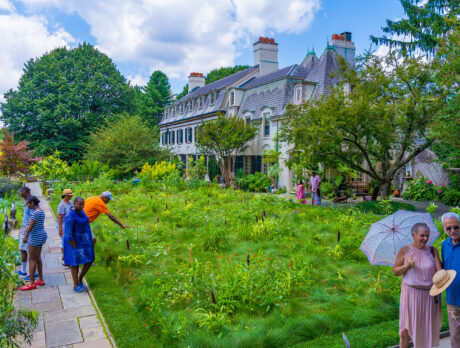 Casually dressed guests explore the lush garden beside the grand historic estate.