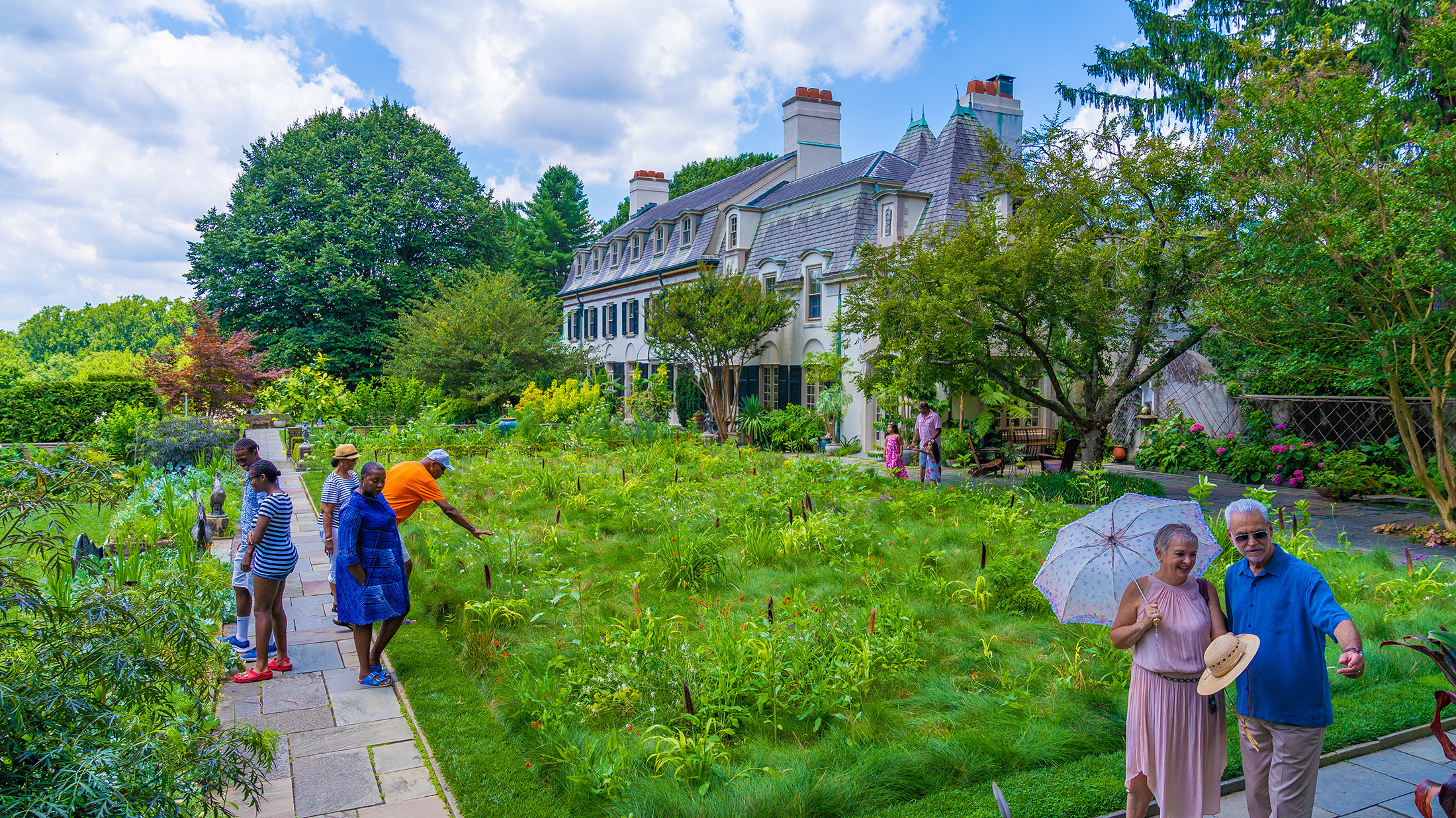 Casually dressed guests explore the lush garden beside the grand historic estate.