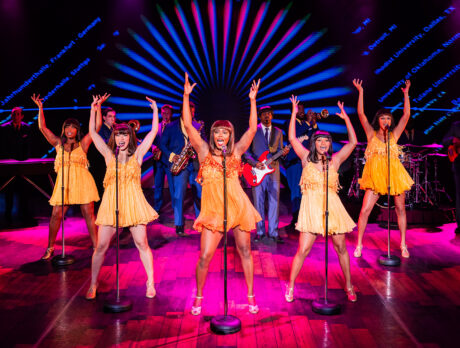 Women dressed in yellow dance on a pink stage for a performance of the Tina Turner musical