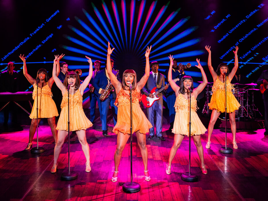 Women dressed in yellow dance on a pink stage for a performance of the Tina Turner musical