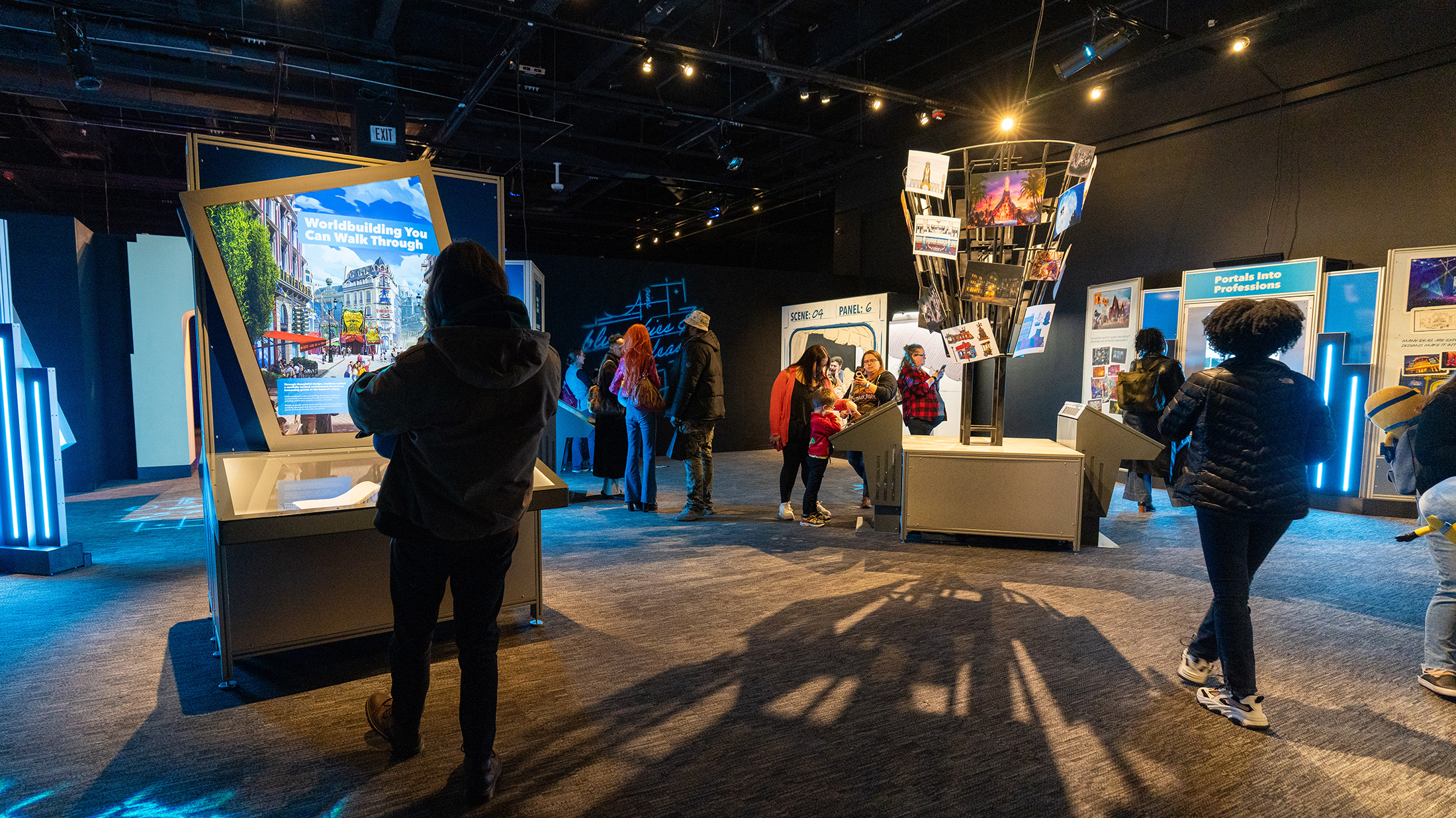 Los visitantes exploran pantallas interactivas y paneles iluminados dentro de la exposición Universal Theme Parks en The Franklin Institute.