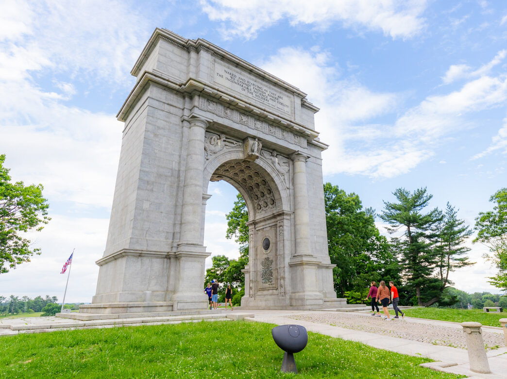 À Valley Forge, les visiteurs se promènent sous une imposante arche de pierre, nichée au milieu d'une pelouse verdoyante et d'arbres feuillus.