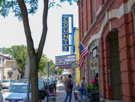 Os visitantes caminham pela Main Street, em Doylestown, passando pelo histórico County Theater, cujo letreiro azul vertical se ergue acima das fachadas das lojas, dos cafés e das bandeiras americanas que se alinham ao longo do movimentado quarteirão do centro da cidade.