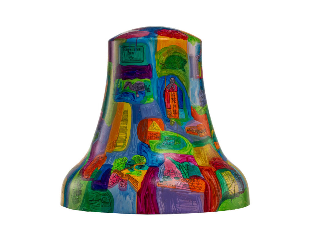 Bell sculpture titled “19128: A Place With Roots” from Philadelphia250’s Bells Across PA, featuring a patchwork of colorful, layered panels depicting scenes and symbols of Roxborough. The design includes small illustrations of landscapes, buildings, signage, and local landmarks arranged in a mosaic of vivid blues, greens, oranges, and purples, highlighting the neighborhood’s history and sense of place.