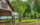 A woman walks her two dogs along the waterfront at Bristol Waterfront Park. The white and red pavilion is boarded by lush green trees.