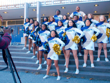 A photographer points a camera at a cheerleading team posing on the steps outside of George Washington High School.