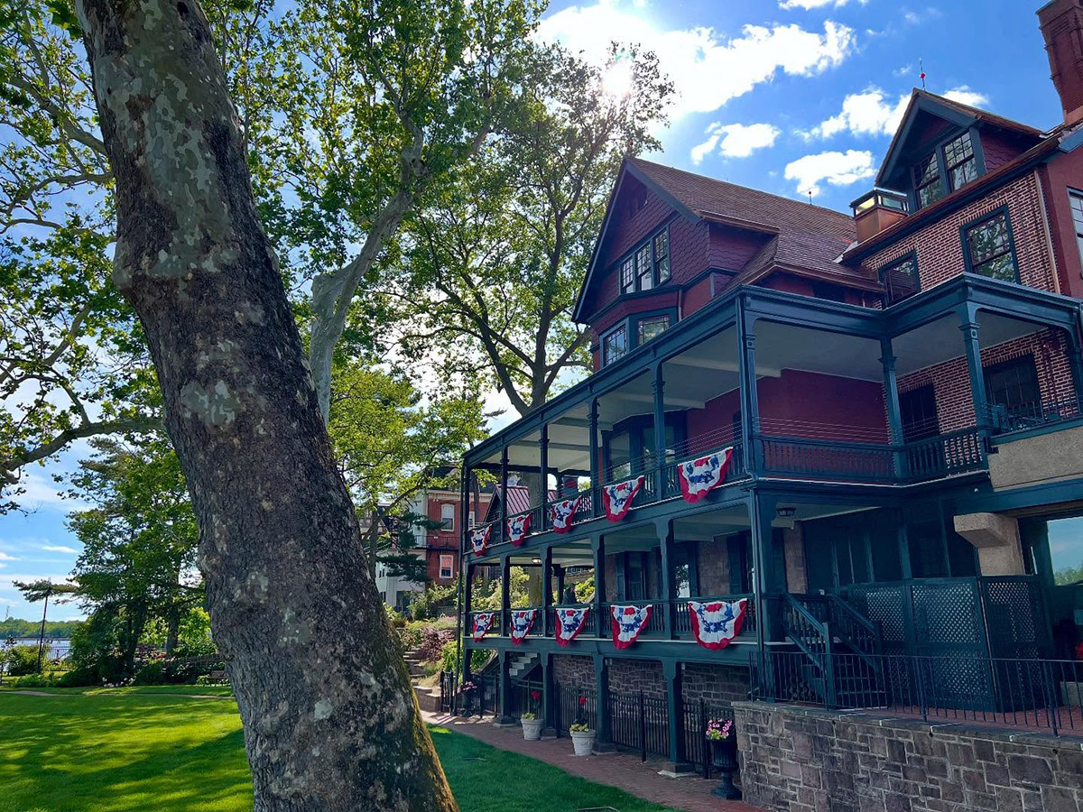A look at the facade of The Grundy Museum. The three story building is decorated with red, white and blue bunting and is shaded by a large tree.