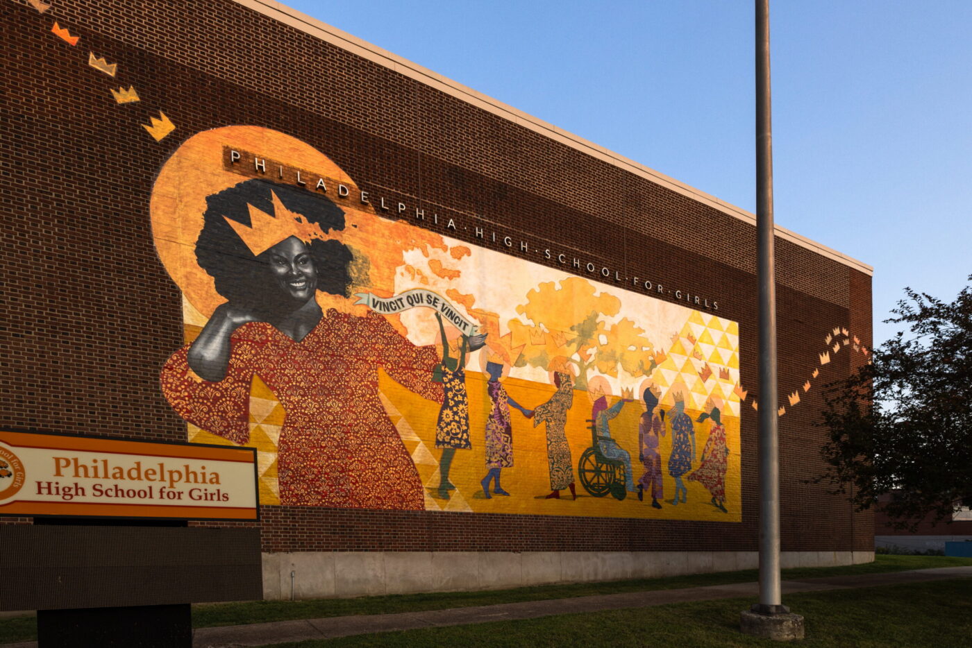 “Luminaries: The Coronation” mural featuring singer Jill Scott on the exterior of Philadelphia High School for Girls, showing Scott wearing a crown and surrounded by stylized figures and golden geometric patterns.