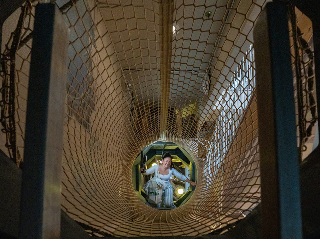 A visitor crawls through a netted tunnel inside the Ministry of Awe immersive experience.