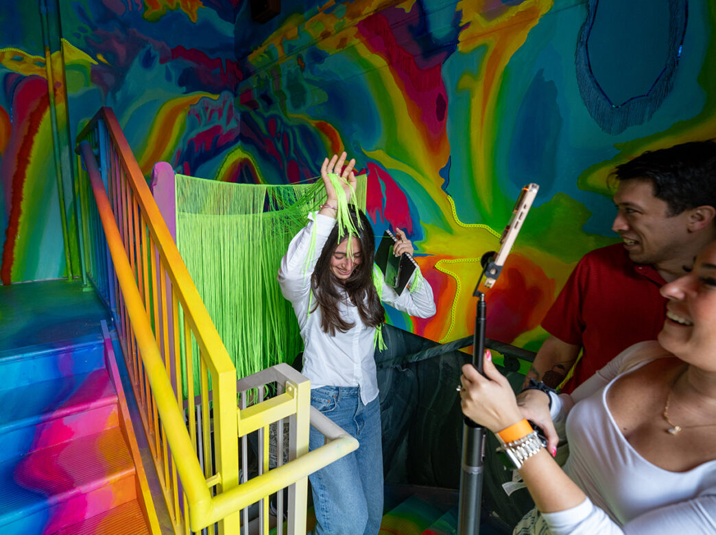 Un visitante se ríe mientras atraviesa una cortina de hilos de color verde brillante dentro de una sala pintada con colores vivos en el Ministerio del Asombro.