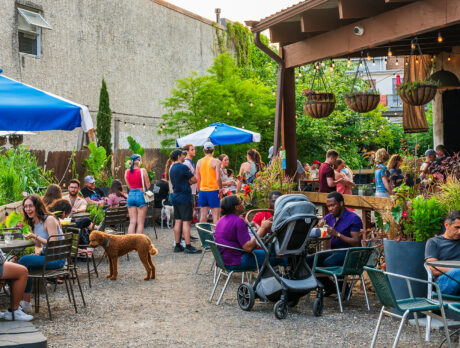 People enjoy drinks and bites in a lush garden setting at the PHS Pop Up Garden on South Street. The garden is complete with shaded tables and hanging planters.