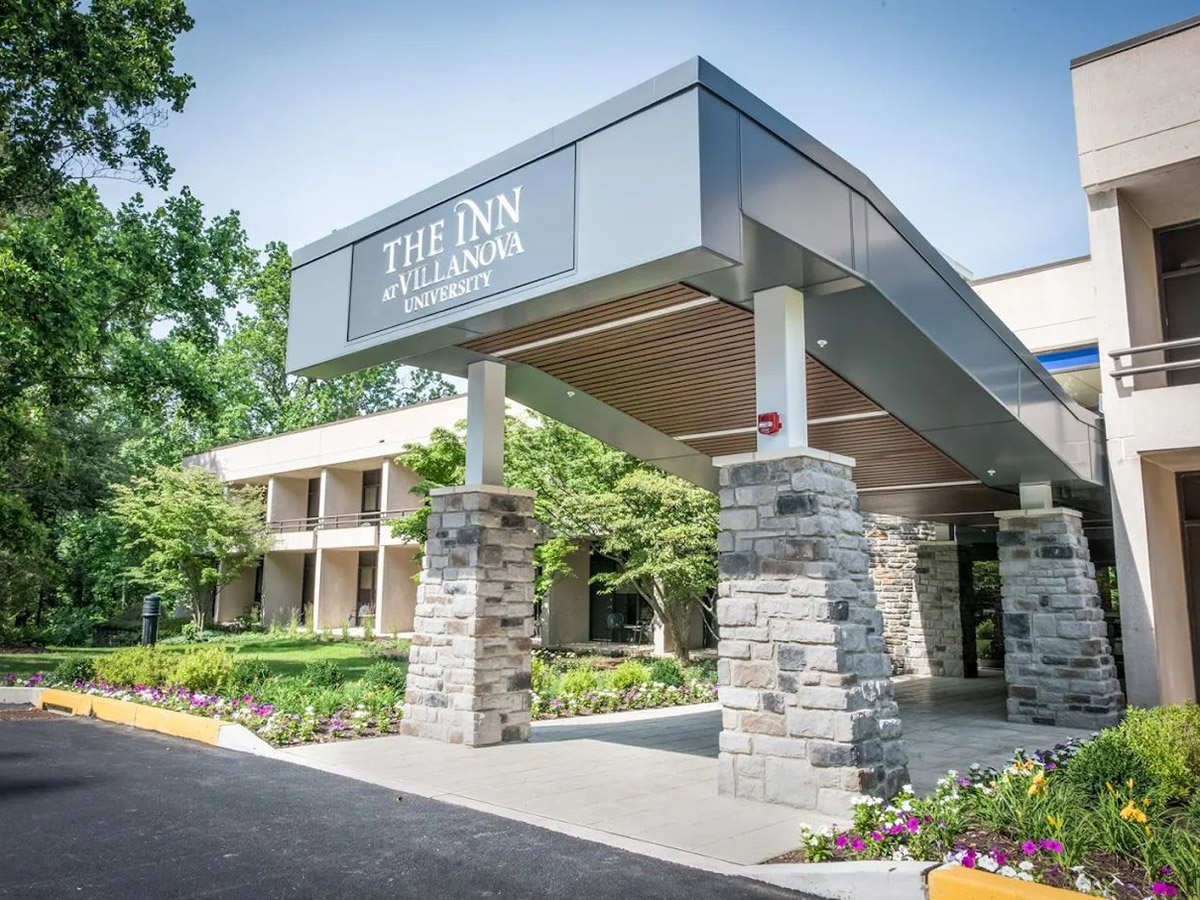 The entrance of The Inn at Villanova University, surrounded by blooming flowers and full trees.