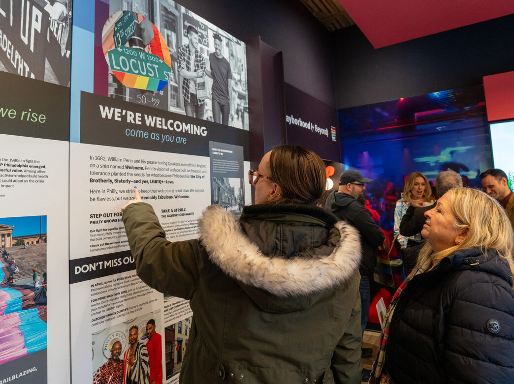 A visitor points at a display panel inside of the Philly Pride Visitor Center.