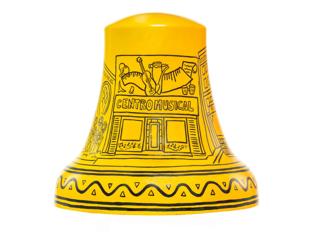 A bright yellow Liberty Bell sculpture titled ‘El Centro de Oro’ features black line illustrations of a neighborhood music shop labeled ‘Centro Musical,’ with instruments, cultural motifs, and decorative patterns representing the Philadelphia community.