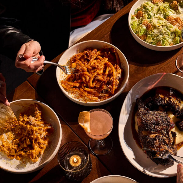 Hands reach across a table to share plates of pasta, roasted chicken and Caesar salad alongside cocktails and wine at Piccolina.