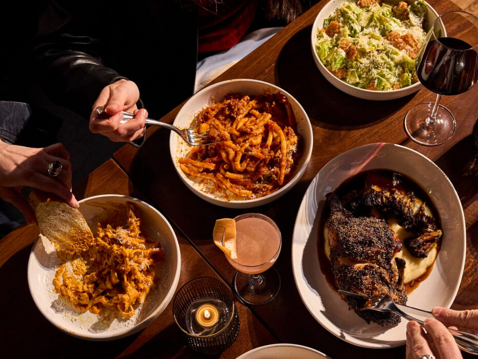 Hands reach across a table to share plates of pasta, roasted chicken and Caesar salad alongside cocktails and wine at Piccolina.