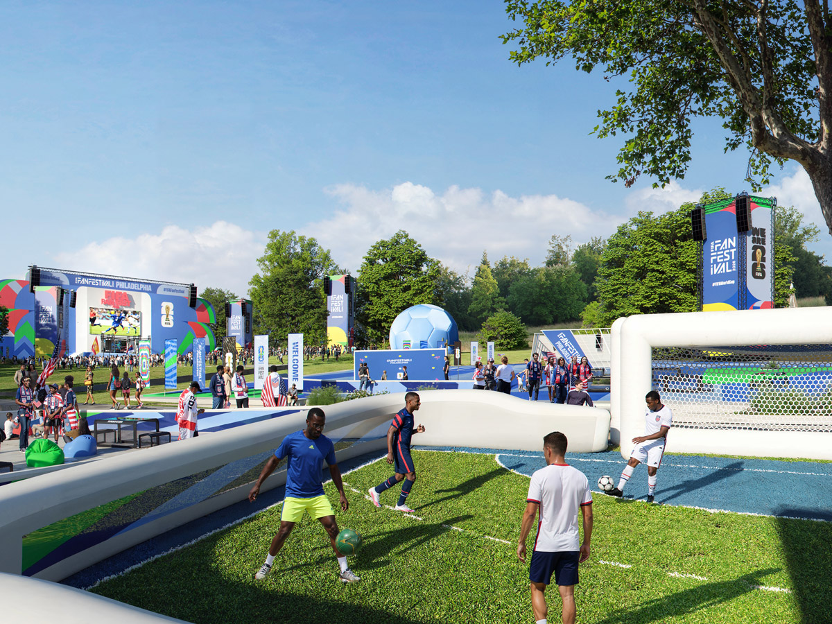 Visitors play a casual soccer game on a small field at the FIFA World Cup 2026 Fan Festival in Philadelphia, with crowds, interactive activities, and a large viewing stage visible in the background.