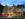 Evening view of Hotel Fiesole in Skippack, Pennsylvania, a warmly lit brick building with outdoor dining umbrellas, trees, and a vintage trolley along the side.