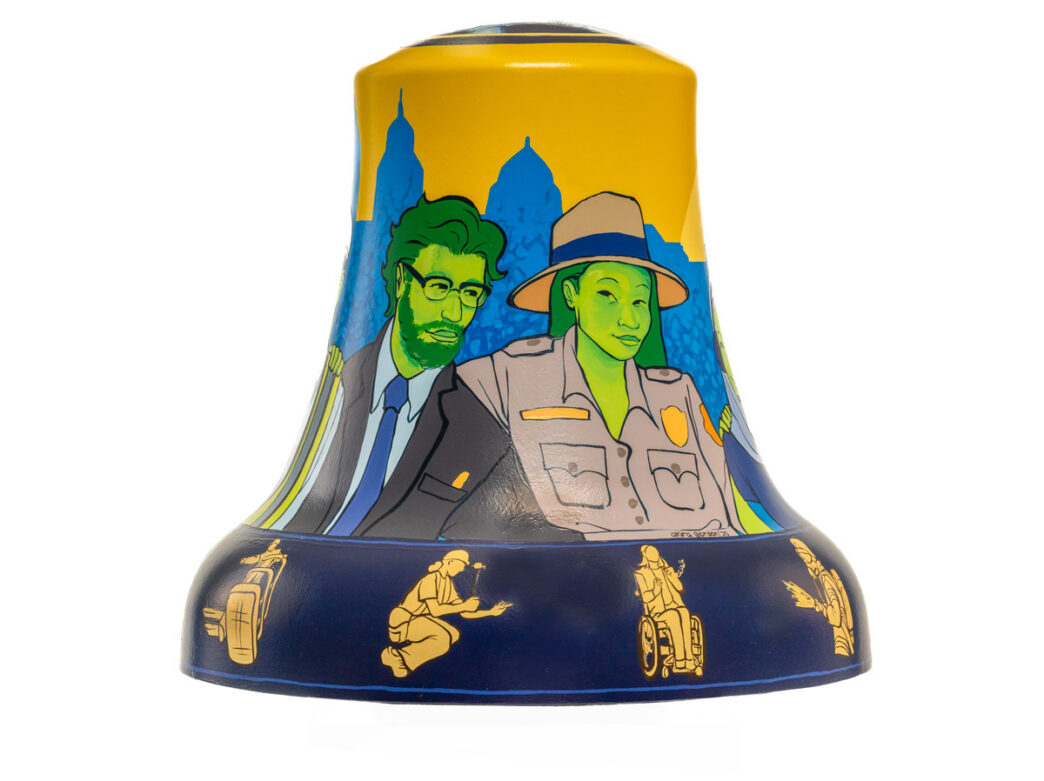 Bell sculpture from Philadelphia250’s Bells Across PA titled “Philly Workforce: Celebrating Our Past, Building the Future,” featuring illustrated figures representing public service workers. A park ranger in uniform and a suited professional stand in front of a stylized Philadelphia skyline, with smaller gold silhouettes around the base depicting various workers, including a person using a wheelchair and others in service roles, set against bold yellow and blue backgrounds.