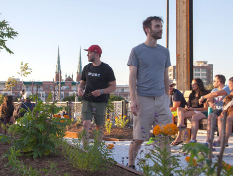 Visitors walk and relax on benches near plants at the Rail Park in North Philadelphia, with city buildings and church spires visible in the background.