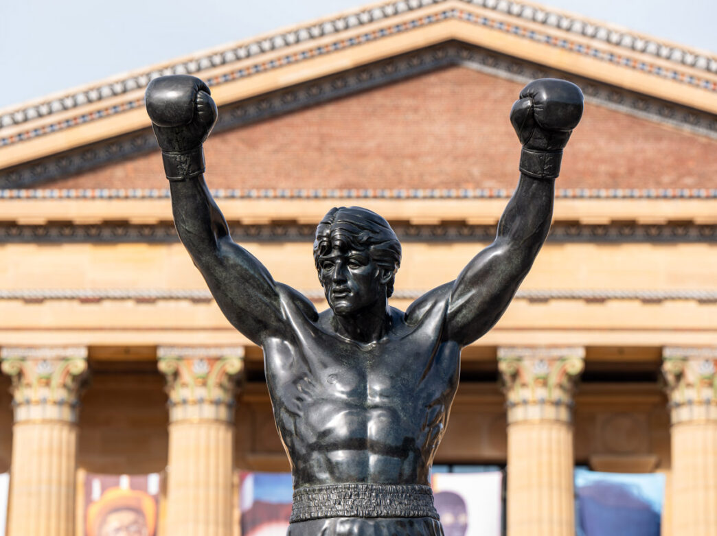 A close-up of the Rocky Statue with the Philadelphia Museum of Art in the background.