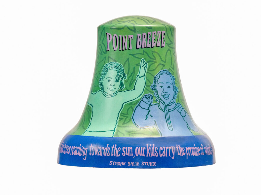 Bell sculpture titled “The Promise of What’s to Come” from Philadelphia250’s Bells Across PA, featuring line-drawn portraits of two children against a green background with leafy patterns. The words “POINT BREEZE” appear at the top, while a quote along the base reads, “Like trees reaching towards the sun, our kids carry the promise of what’s to come,” emphasizing youth, growth, and community hope.