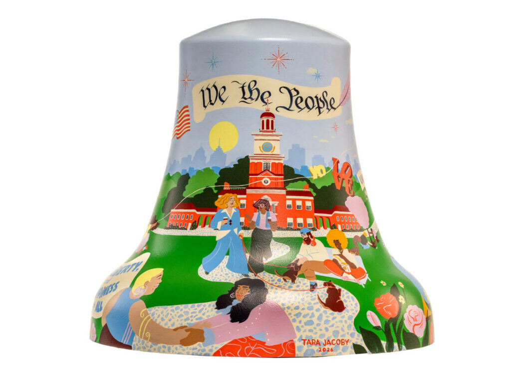 A decorative Liberty Bell sculpture titled ‘We The People’ features a colorful illustration of Independence Hall surrounded by diverse people, greenery, and patriotic elements on a light blue background.