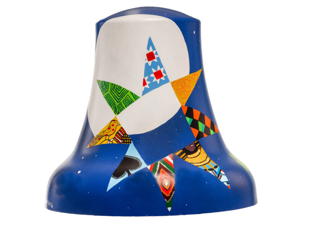 Bell sculpture titled “Who’s Your North Star” from Philadelphia250’s Bells Across PA, featuring a large white star shape against a deep blue background. The star is composed of colorful patterned segments, including geometric designs and textile-inspired motifs, with additional star points extending outward along the base, evoking guidance and diverse cultural influences.