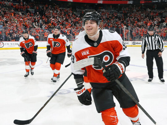 Several Philadelphia Flyers players skate off the ice while smiling.