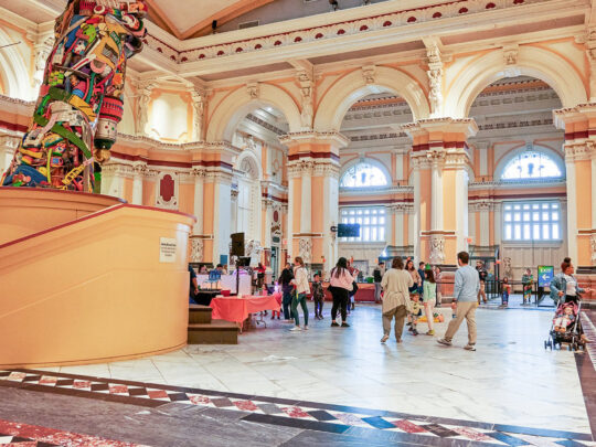 A crowd of visitors walk on a marble floor inside the Please Touch Museum.