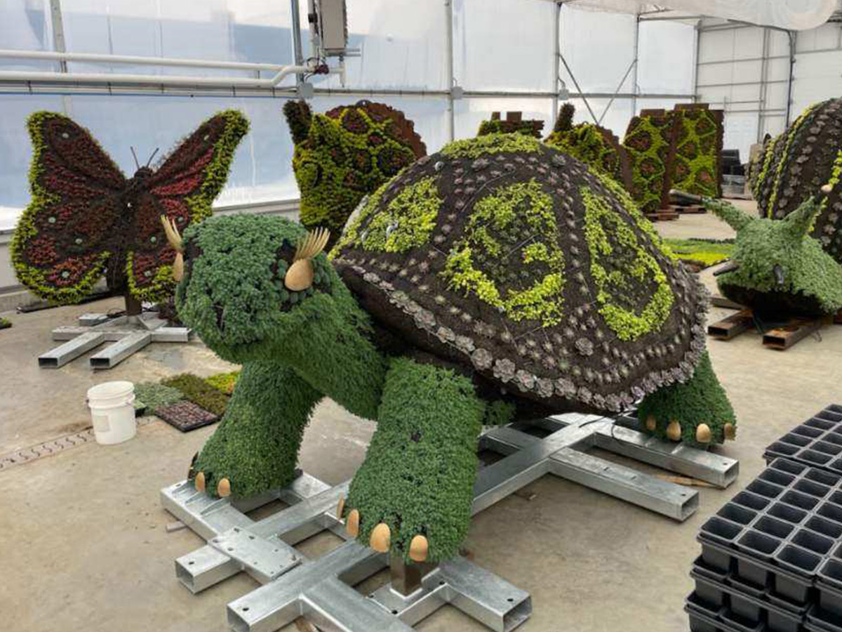 A large topiary art piece is shaped like a giant tortoise. Several other animal-shaped topiaries are visible in the background.