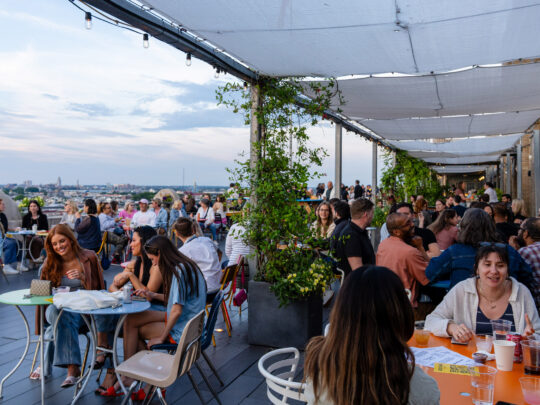 People sit and enjoy drinks at the Bok Bar in South Philly, with a view of the city in the background.